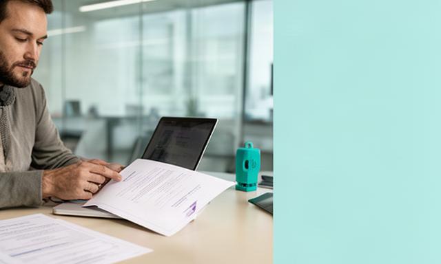 Technology consultant reviewing a printed service agreement beside a laptop in a modern Stockport office